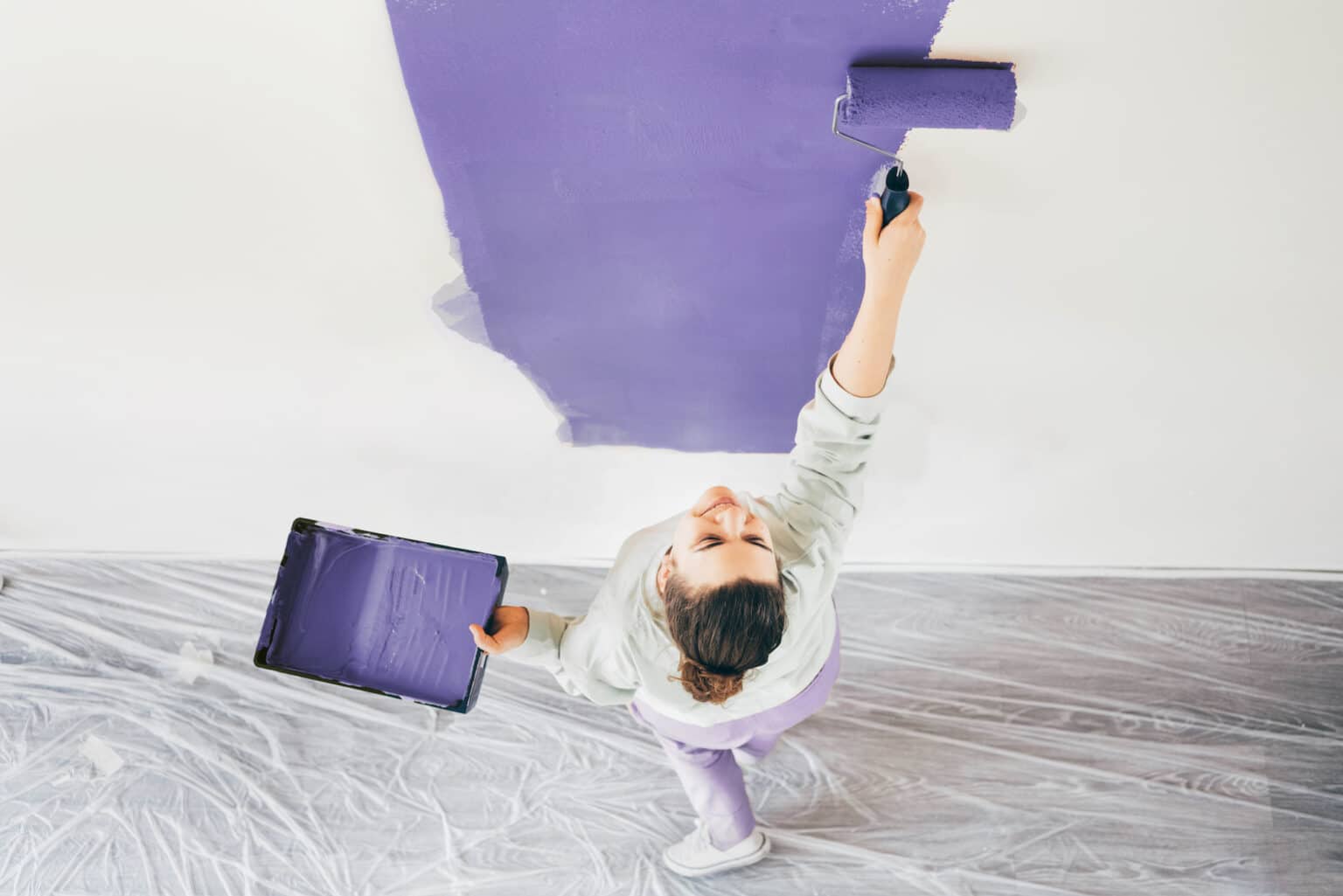 Funny woman painting wall. Woman with paint roller painting wall. Repair and house renovation concept.